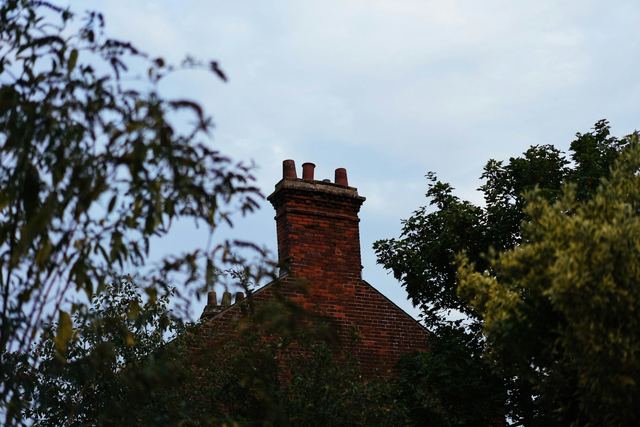 A red brick chimney rising above a roofline between leafy trees